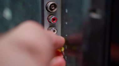 Hand inserts rca connectors of red white and yellow color from tv. Plug tulip of the old generation close-up. Wires for transmitting audio and video signals are thin, poor quality. High quality 4k