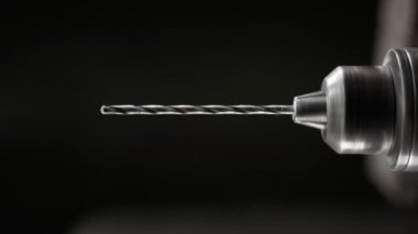 Rotation of a drill for metal in slow motion close-up on a black background. Metal rod in a drill chuck. Industrial background of a screwdriver with a drill in dark colors. professional tools. High