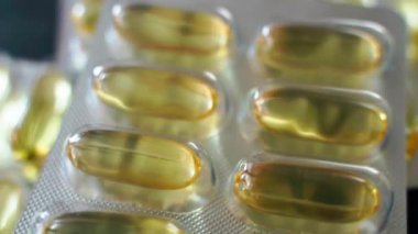 Balık yağı kapsüllü parlak kabarcıklar yakın çekim dönüşümlü. Jelatin kabuklu ve sarı geniş kapsüllü haplar. Tedavi araçları ve sağlığın korunması. Omega 3 ve Omega 6 'nın kaynağı. Yüksek