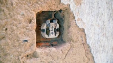 Kil bir duvarda eski sökülmüş bir soket. Kırsal kesimdeki eski bir evde elektrik tesisatı çok kötü durumda. Parçalanmış elektrik prizleri ve seramik kaplamalı terk edilmiş bir ev. Yüksek