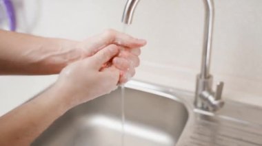Genç bir adam ellerini sabunlu suyla dikkatlice yıkıyor akmakta olan suyun arka planına yakın çekim yapıyor. Sokaktan sonra ellerini yıkıyorsun. Kişisel hijyene ve cildinizin sağlığına dikkat edin.