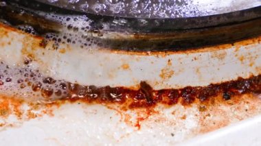 Yanmış kaplamalı eski, kirli bir mutfak elektrikli sobası bol miktarda deterjan köpüğü ve kimya ile doludur. Kıvrımlı kirliliğe sahip dağınık, modası geçmiş bir ocağa yakın çekim. Spreyli yağ lekeleri