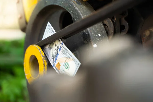 One hundred dollar bill close-up against the background of the engine of a rural walk-behind tractor. Money in the driven pulley on the belts