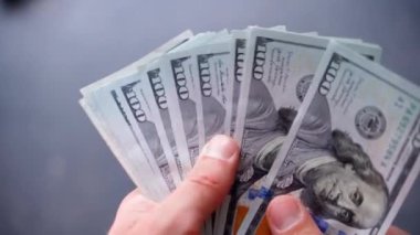 Parmaklar, bulanık gri arka plandaki yüz dolarlık banknotları hızla sayıyor. Büyük bir meblağ için zor bir veda. Bankada büyük bir kredi satın alma ya da ödeme. Taze dolar