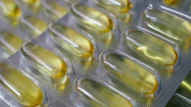 Bir ışık parıltısı, balık yağı kapsülleriyle su toplamasını aydınlatır. Şeffaf plastik ambalajlı sarı jelatin tabletler. Yüksek kalite 4k görüntü