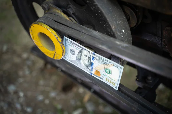 Hundred dollar bill close-up on an industrial background. Money on a belt driven tractor engine pulley. Production costs and the financial component of big business