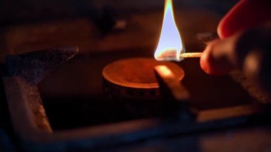 Benzin ocağında kibritle birlikte ateşleniyor. Düşük kalite gaz, yakın çekim için yeterli değil. Karanlıkta elinde kibrit olan bir el mutfak sobasına getirilir. Borulardaki mavi yakıtın kalıntıları. Yüksek
