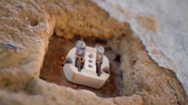 Eski bir kil duvarda, bir duvar prizinin çıplak iç kısımlarına yakın çekim. Parçalanmış bir elektrik prizinin seramik gövdesi. Kırsal bir evde eski elektrik kabloları. Pürüzsüz kamera hareketi. Yüksek kalite FullHD