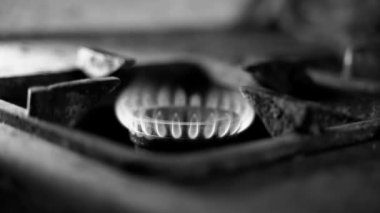 Acınası bir durumdaki eski bir gaz ocağının ocağında kararsız bir gaz patlaması. Kırsal bir gecekonduda yanan mavi bir yakıtın siyah beyaz videosu. Düşük yaşam kalitesi, yoksulluk ve ısınma