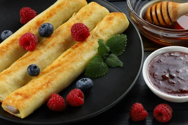 Pancakes rolls with honey and berries. Traditional thin pancakes or crepes with honey and raspberries