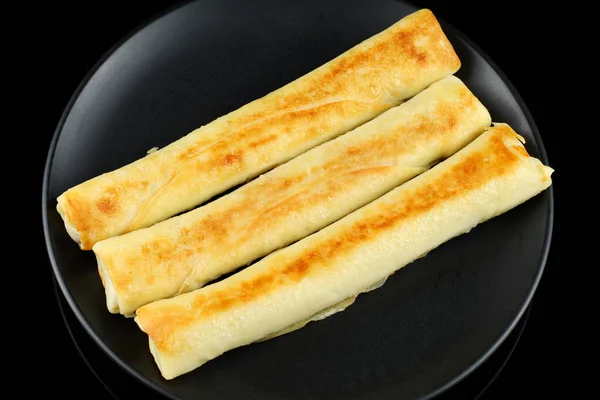 Pancakes rolls on a black plate. Stuffed thin pancakes rolled