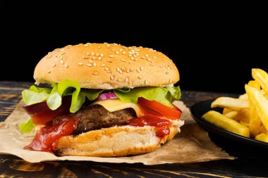 Pirzola, domates, peynir ve sebzeli hamburger. Siyah arka planda izole edilmiş taze lezzetli burger.