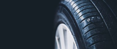 Yakın plan, keskin metal bir vidanın otomobil lastiğini, siyah arka planı ve kopyalama alanını deldiğini gösteriyor.