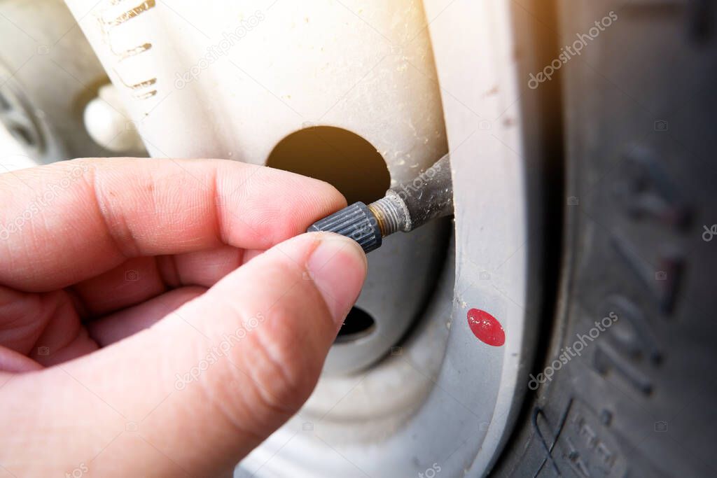 The auto mechanic hand puts on the tire valve cap of a car wheel
