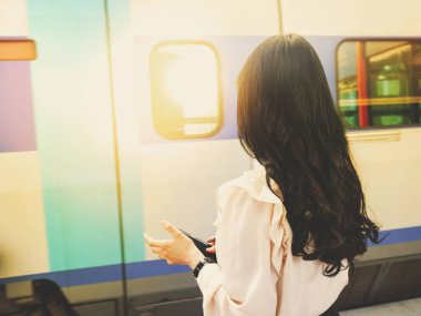 Long-haired Asian woman standing with her back waiting for a train at a high-speed train station to go to work