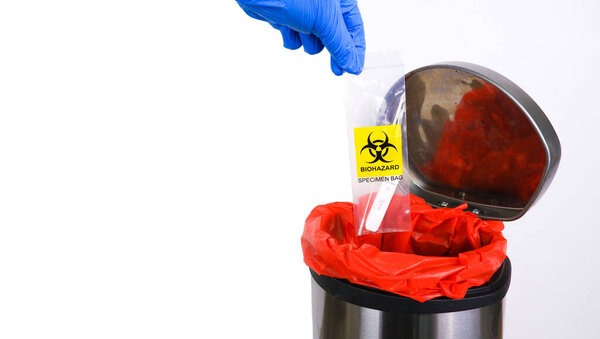 Infectious garbage is being thrown into the red infectious waste bin by the doctor hand with a copy space on white background 