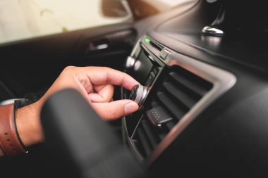 The driver hand adjusts the volume on the dashboard of the car radio.