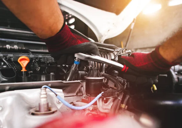 The red gloved hand of the auto mechanic is fastening the bolt with the socket wrench to fix the vehicle engine.