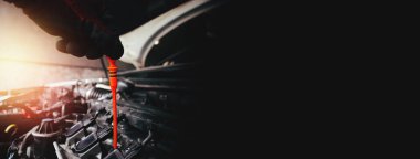 Otomobil tamircisi, yanma motorunun motor yağı seviyesini kontrol etmek için turuncu dipçubuğu çekiyor. Siyah arka planda fotokopi alanı olan yatay pankart, otomobil bakım hizmeti konsepti.