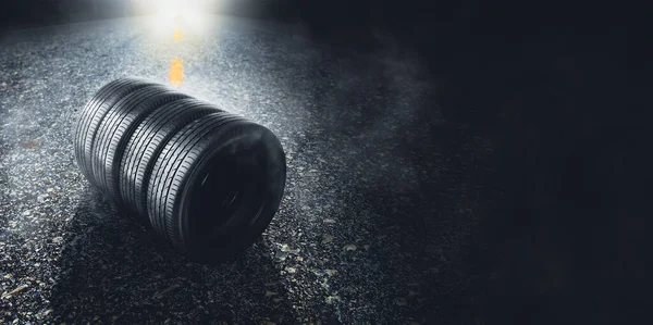 Car tyre on a paved road with smoke and a car headlight on the background at night , panoramic banner copy space on black background