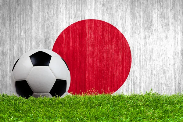 Футбольный мяч на траве на фоне японского флага — стоковое фото