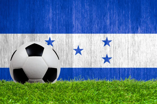 Balón de fútbol sobre hierba con fondo de bandera de Honduras — Foto de Stock