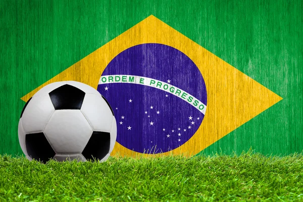 Balón de fútbol sobre hierba con fondo de bandera de Brasil — Foto de Stock