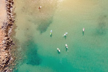 Aerial view by drone of people practicing Stand Up Paddle or SUP in Mediterranean turquoise clear sea.