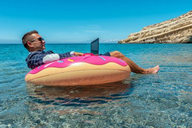 Denizdeki şişme donutta dizüstü bilgisayar kullanan bir iş adamı. Yaz tatili kavramı.