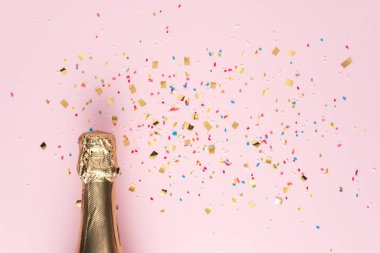 Golden champagne bottle with confetti on pink background. Minimal party concept.