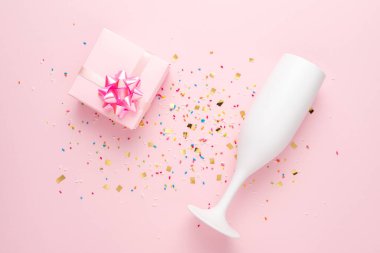 Beyaz şampanya bardağı ve pembe arka planda konfeti olan hediye kutusu. Asgari parti konsepti.