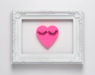 Kalp şeklinde pembe kağıt, beyaz arka planda kirpikleri var. Sevgililer Günü ya da kadınlar için arka plan tasarımı. Minimum düzlük.