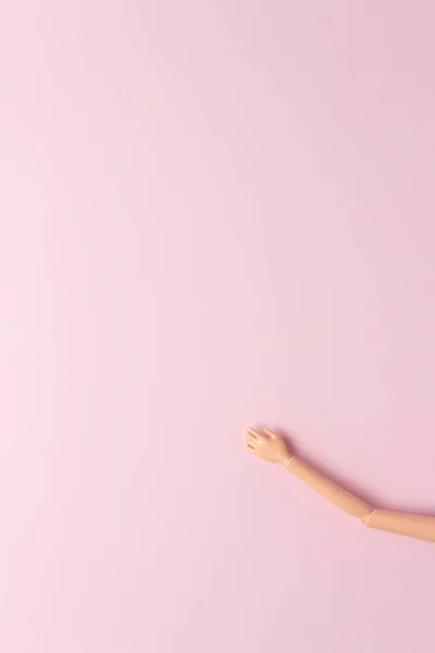 Hand of a doll on empty pink background. Minimal concept.