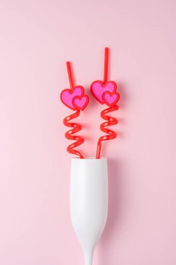 Pembe arka planda bir kamışın üstünde kupa olan beyaz bir şampanya kadehi. Aşk minimum konsepti.
