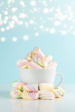 Marshmallow 'lar mavi bokeh arka planda bir fincanda renkli sakızlı şekerler. Tatlı bayram yemekleri konsepti.
