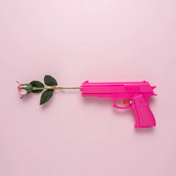 Pink handgun on pink pastel background with rose flower. Minimal flat lay concept.