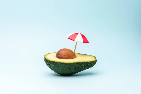 Tropical beach concept made with avocado fruit and sun umbrella. Creative minimal summer background.