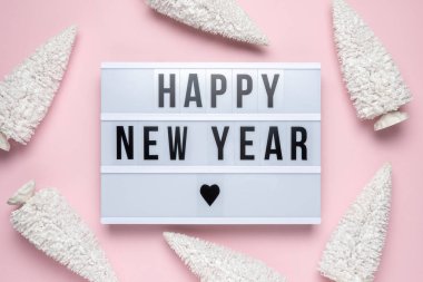 White christmas trees with lightbox with text HAPPY NEW YEAR on pink background. Minimal holiday concept.