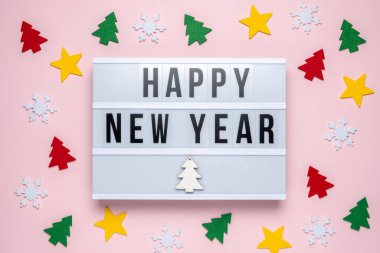 Colorful christmas decor and lightbox with text HAPPY NEW YEAR on pastel pink background. Minimal Christmas or New Year holiday concept.