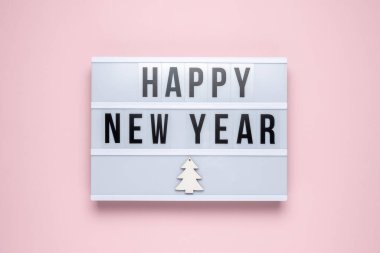Pastel pembe arka planda Mutlu Yıllar yazılı ışık kutusu. Asgari Noel veya Yeni Yıl konsepti.