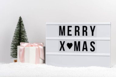 Christmas tree, gift box and lightbox with text MERRY XMAS on a table with snow. Minimal Christmas or New Year concept.