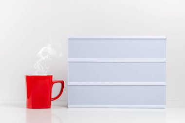 Beyaz masada boş ışık kutusu olan kırmızı kahve fincanı. Model konsepti.