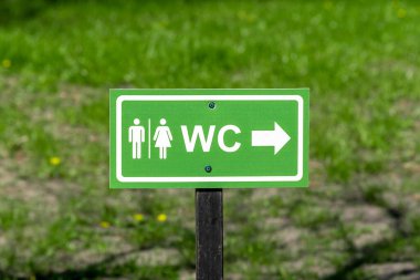 WC logo, sign of public toilets on the street against grass background. 