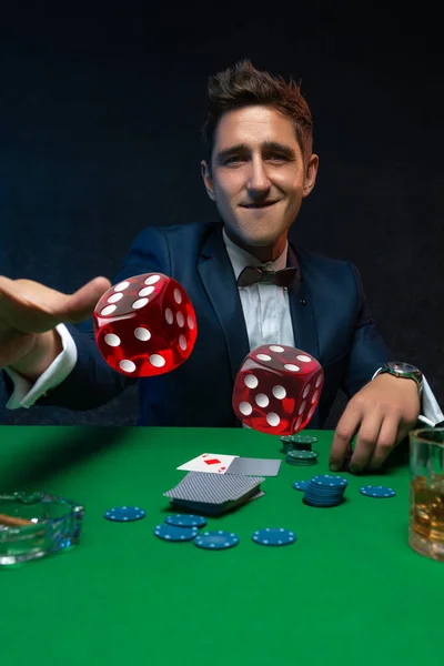 Happy casino player throwing a dice at green table in casino.