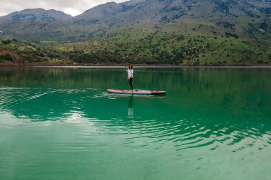 Göl kenarında Stand Up Paddle ya da SUP çalışan bir kadının hava görüntüsü.