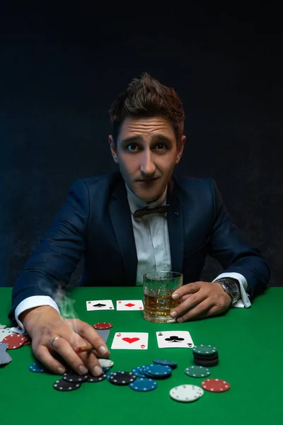 Poker player with cards and chips at green table in casino.