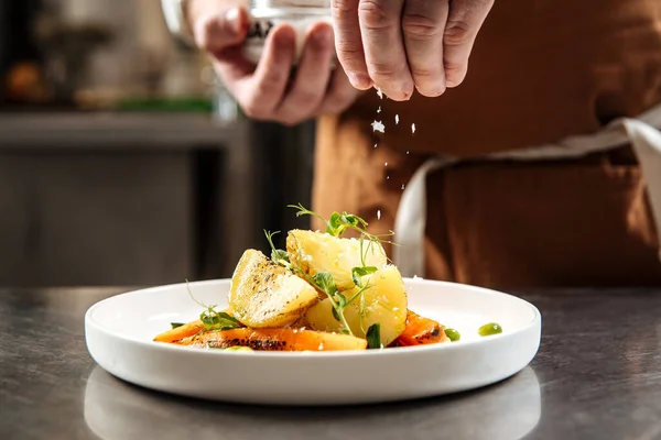 Chefs hand sprinkles cooked dish with salt — Stock Photo, Image