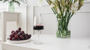 Beyaz masada üzüm ve vazo ile bir kadeh kırmızı şarap.