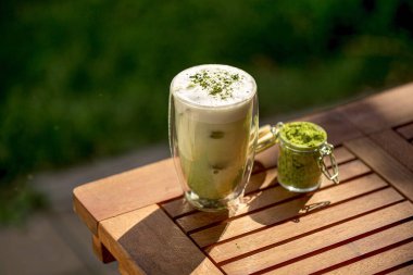 Bahçedeki ahşap masada bir fincan yeşil kibrit latte.