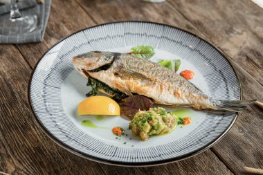 Ahşap arka planda ızgara gurme balığı tabağına yakın plan.